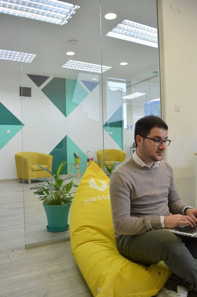 A person sitting on a bean bag in an office and typing on a lap top