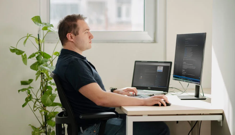 A person working in front of a lap top an an additional monitor in an office